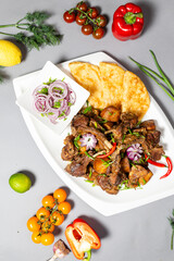 Top view of braised ribs with flatbread and onions on grey background.