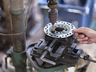 Focused mechanic using drill press machine for metalworking in workshop. hand holds steel disc for drilling, creating hole for custom repair work