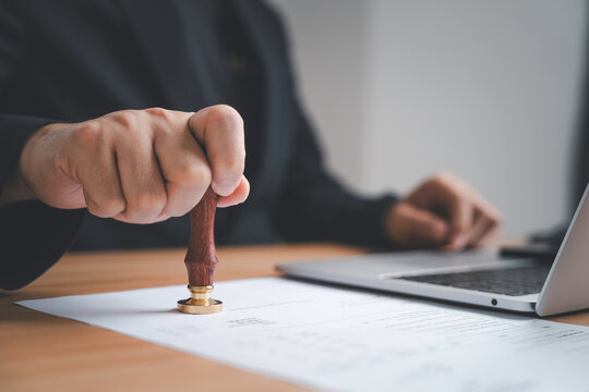 Businessman hand pressing a seal stamp on a document symbolizing authorization validation accuracy and official confirmation in professional business processes as an approval stamp concept