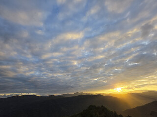 Fototapeta premium Beautiful sunrise over mountain range. tranquil golden light from sun illuminates scenic sky filled with clouds. peaceful morning nature landscape with sun rays