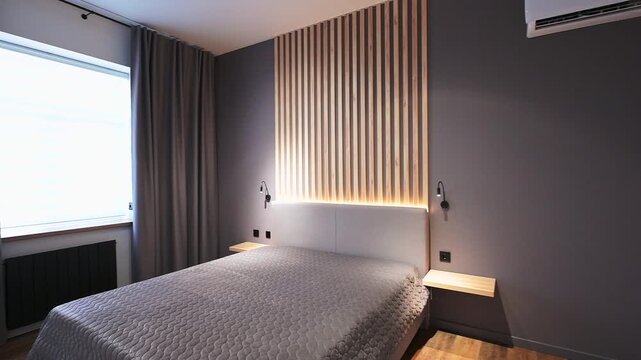 Modern bedroom with a grey bed, wooden slat accent wall, and floating nightstands. Grey walls, wood floors, and an AC unit complete the sleek, cozy design