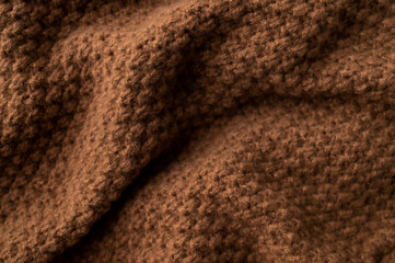 Texture of knitted brown wool-cotton sweater. Soft, cozy, warm, winter or fall garment features a large interwoven pattern, ornament. Close-up of the garment. Trendy Color of the Year 2025