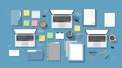 Top view of modern office workspace with laptops, notebooks, coffee, and stationery on blue desk