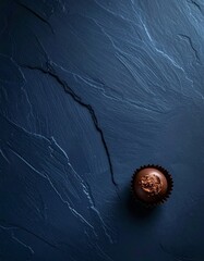 マットなディープネイビー背景の右下に、高級チョコレートプラリネを一粒配置した構図です。
