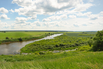 Summer landscape with a winding river and green fields under a cloudy sky