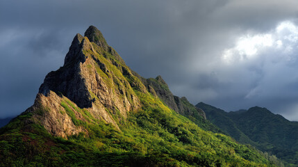 Majestic mountain peak covered in lush green vegetation rises dramatically against a backdrop of dark, moody storm clouds in a breathtaking landscape view.