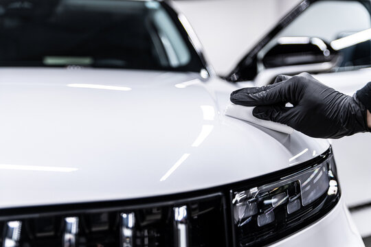 Close-up of ceramic coating being applied by a gloved detailer to a white car hood and front body panel, showing precision work, paint protection and premium car detailing service.