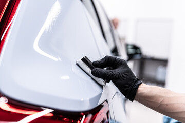 Close-up of ceramic coating being applied to a rear car body panel near the taillight by a gloved detailer, highlighting precision work, paint protection and premium car detailing service.