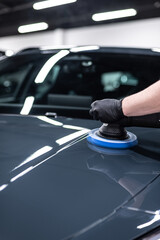 Close-up of machine polishing on a glossy black car hood in a professional detailing studio, showing paint correction process, surface refinement and preparation for ceramic coating.