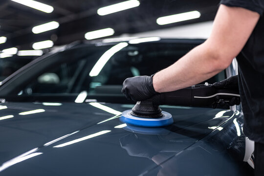 Close-up of machine polishing on a glossy black car hood in a professional detailing studio, showing paint correction process, surface refinement and preparation for ceramic coating.