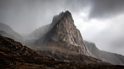 Dramatic rocky mountain peak shrouded in misty fog rises majestically against a cloudy sky creating a scenic and atmospheric landscape of rugged beauty.