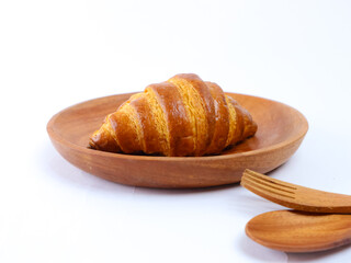 Buttery golden croissant placed on a wooden plate isolated on white background