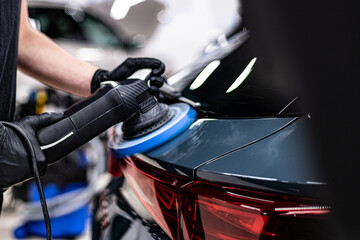 Close-up of machine polishing and paint correction on a car body panel near the rear taillight in a professional detailing studio, improving gloss, surface clarity and paint condition.