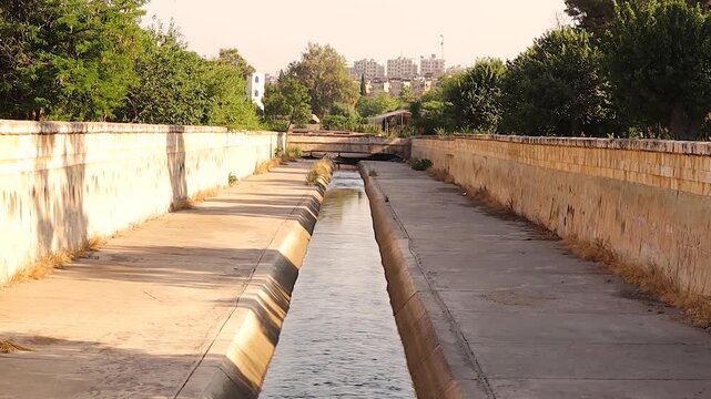 Peaceful view of the Queiq River running through Al-Shahba Public Garden in Aleppo, Syria. This urban nature scene highlights the harmony between water, greenery and city life. Travel, environmental.