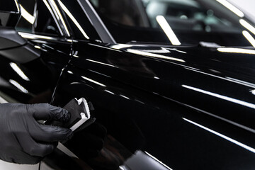 Close-up of ceramic coating applied by hand to glossy black car paint, highlighting deep reflections, precise technique, paint protection and premium car detailing service.