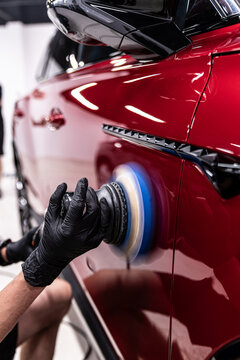 Close-up of machine polishing on a red car body panel, showing paint correction process, surface refinement, gloss restoration and professional car detailing service.