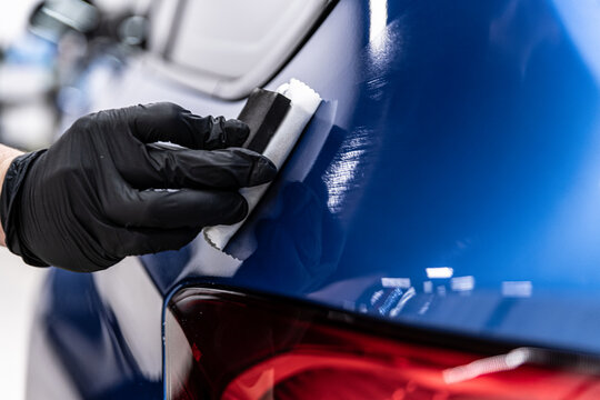 Close-up of ceramic coating being applied to a blue car body panel near the rear taillight by a gloved detailer, highlighting precision work, paint protection and premium detailing service.