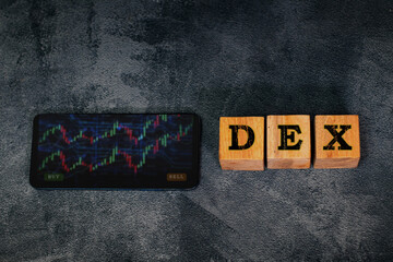 Wooden blocks spelling “DEX” sit beside a smartphone showing a colorful crypto chart, representing decentralized exchange trading, blockchain technology, and modern digital finance trends.