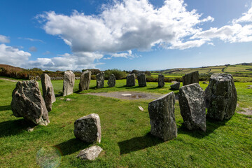 Naklejka premium Small axial Drombeg stone circle or The Druid's Altar at Drombeg, Glandore, Cork, Ireland with 13 stones in megalithic ruins with panoramic landscape and cumulus clouds in background