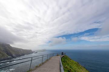 Panoramic high level view over a pathway with some people at the end overlooking the Kerry Cliffs along the coastline of Kerry, Ireland and the North Atlantic Ocean