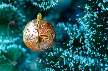 A stunning copper-gold Christmas bauble featuring an embossed reindeer design hanging on a frosted pine tree. This elegant ornament adds a classic touch to the festive holiday decor. © Sony Herdiana