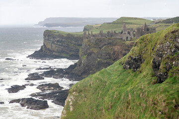 Rugged West coast of Ireland during storm with high waves and now-ruined medieval Dunluce Castle at the edge of the cliff overlooking the ocean