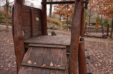 Wooden children's playground structure in an autumn park with fallen leaves. Rustic outdoor play equipment for kids in a public garden or backyard. Natural wood playhouse.