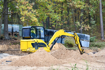 Mini excavator at construction site surrounded by trees. Compact construction equipment for operative earthworks. Tracked yellow and black mini excavator digger.