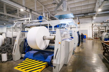 A large production machine with a large spool of white fabric, which are used in textile production.