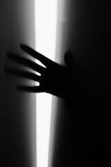 Czarno-białe zdjęcie przedstawiające cień dłoni na ścianie. Pionowy pas światła biegnie przez środek, z ciemnością po obu stronach, a dłoń częściowo wnika zarówno w jasne, jak i ciemne obszary. © Elżbieta Kaps