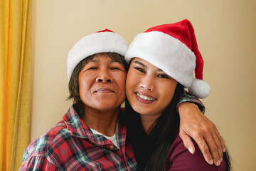 Portrait of asian mother and daughter wearing santa claus hats and celebrate Christmas together at home - Xmas, holiday, and thai family concept