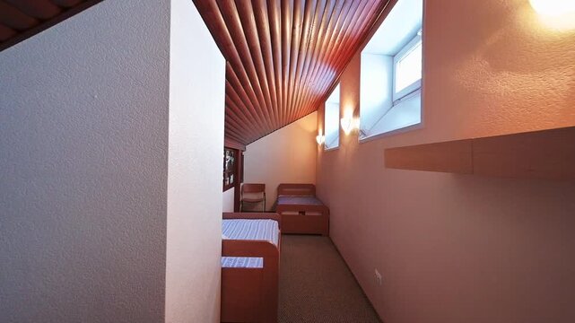 Compact bedroom with two single beds, a unique slatted wooden ceiling, and stained-glass windows. Warm lighting creates a cozy, intimate atmosphere