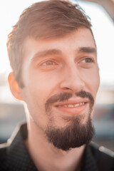 Fototapeta premium Close-up portrait of a young bearded man outdoors in warm sunlight, looking to the side with a calm expression. Shallow depth of field and natural lighting