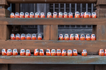 Rows of traditional daruma dolls placed on wooden shelves in a historic building in Japan during daylight hours
