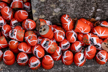 Daruma dolls stacked in a pile near a stone wall during a festival celebration in Japan at night