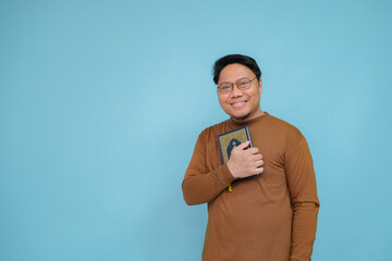 Portrait of an Asian Muslim man carrying the holy book of the Koran wearing brown shirt and glasses, let's always read the holy book of the Koran
