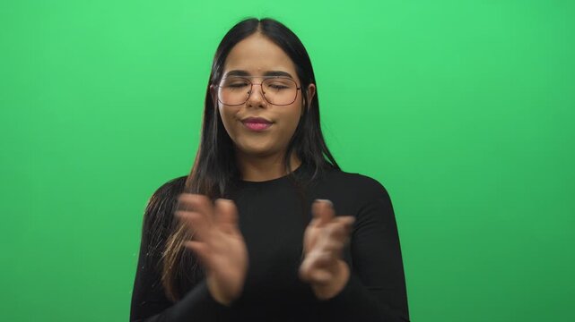 Woman hands clapping unfold on a green set featuring a young latin hispanic model isolated against a seamless background wall.