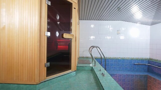 Modern spa area featuring a wooden sauna with glass door next to a tiled indoor pool. Clean, serene environment for relaxation and wellness