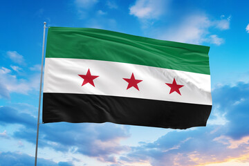 The Syrian independence flag waves dynamically against a bright sky, showing its green, white, and black stripes with three vivid red stars. Sharp lighting and clear motion 