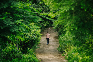 A lone figure runs down a dirt path through a lush, green forest. The path leads into the distance, framed by dense foliage. It evokes a sense of solitude and journey.