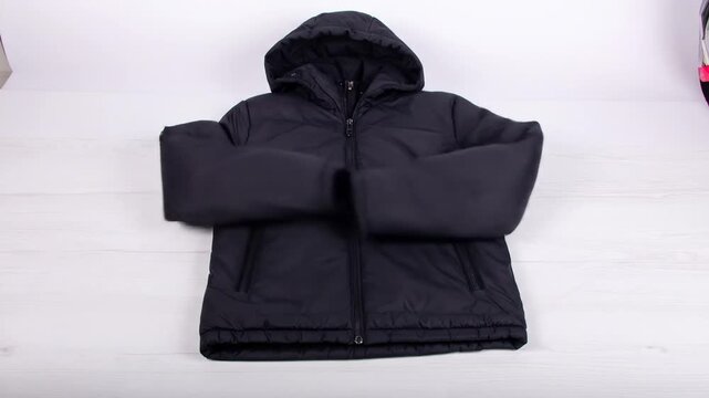 A black, quilted jacket with a hood, zippered front, and pockets, laid out on a white surface