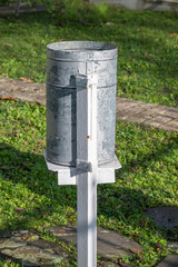 Fototapeta premium A cylindrical rain gauge stands on a white frame in a grassy outdoor area for weather measurement.