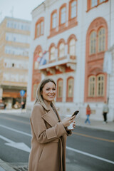 Fototapeta premium Smiling woman with phone enjoys city stroll near historic building