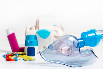 Face mask of modern nebulizer on white table. Equipment for inhalation, close-up, selective focus, white background. Asthma breathing treatment. Bronchitis, asthmatic health equipment.