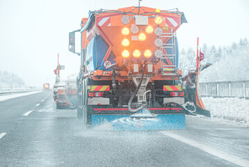 Snow plow sprinkles highway with road salt in freezing weather.