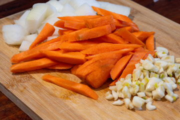 Diced onions, julienned carrots, and minced garlic are neatly arranged on a wooden cutting board for cooking.