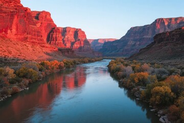 Sunset over a canyon with a calm river reflecting red rock formations and autumn foliage