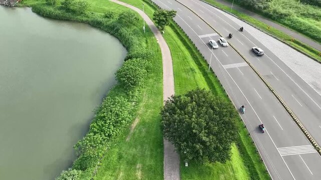 Aerial view of a riverside park next to a busy highway, showcasing the contrast between nature and urban infrastructure