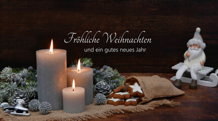 Weihnachtskarte: Romantische Dekoration mit brennenden Kerzen, Weihnachtskugeln und Tannenzweigen vor einem Holzbrett. Auf dem Holz steht der Gruß frohe Weihnachten und ein gutes neues Jahr.
