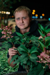 Man in black hoodie peeking from behind dark green foliage